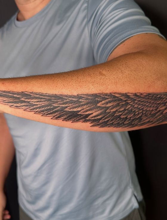 Black feather texture tattoo across a forearm