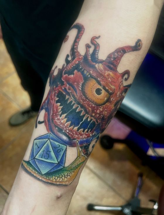Color monster tattoo with a large eye above a twenty-sided die