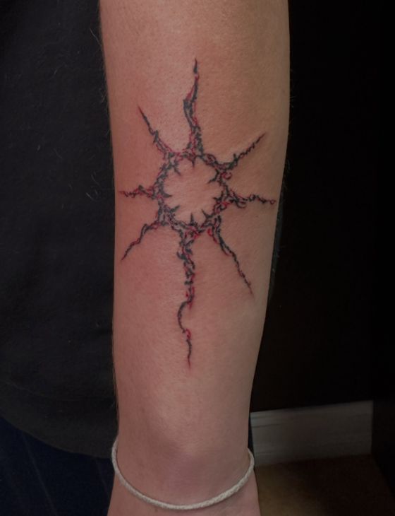 Red linework sun tattoo on a forearm